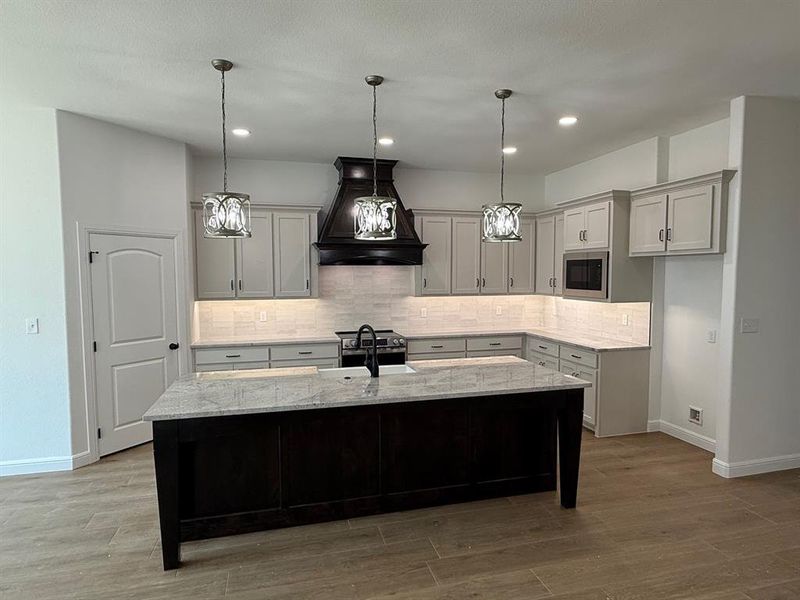 Kitchen with custom range hood, tasteful backsplash, light stone countertops, a kitchen breakfast bar, and a 9 foot island with seating