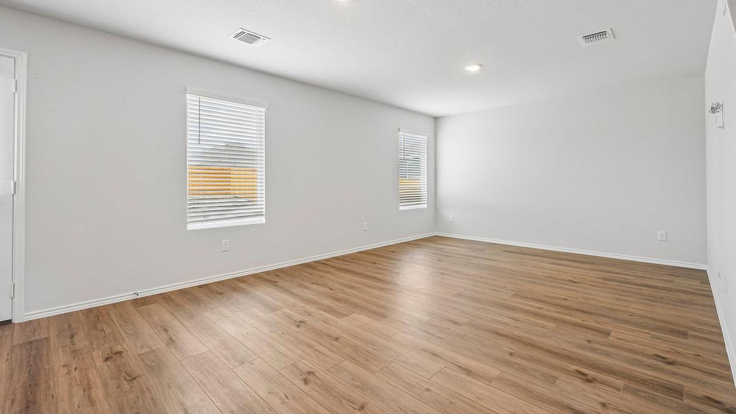 Recessed lighting illuminates this versatile room featuring durable wood-look flooring and multiple window views.