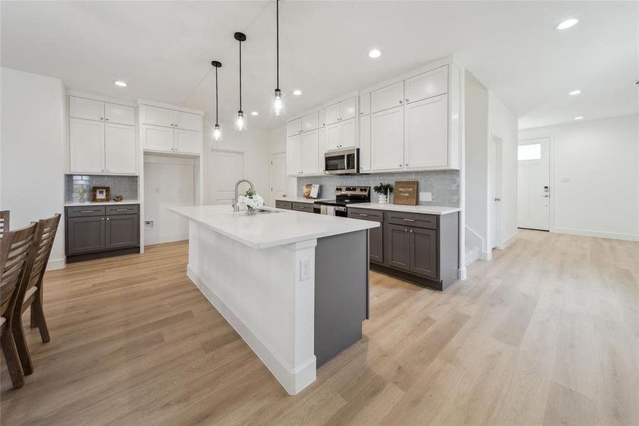 Kitchen featuring appliances with stainless steel finishes, an island with sink, sink, gray cabinetry, and light hardwood / wood-style flooring