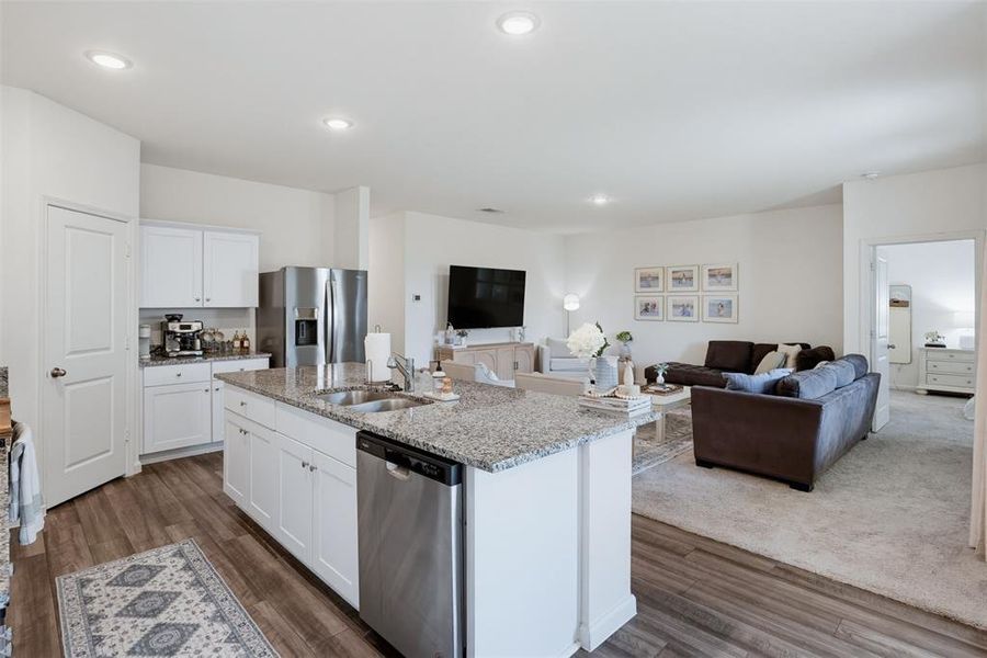 Open-concept living space featuring a kitchen island with integrated sink, stainless steel appliances, white cabinetry, and wood-finish flooring
