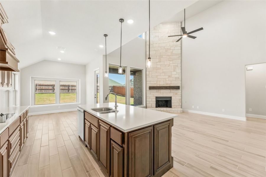 Open kitchen with center island, dark wood cabinets, and stone fireplace in adjoining living area with vaulted ceiling Open kitchen with center island, dark wood cabinets, and stone fireplace in adjoining living area with vaulted ceiling