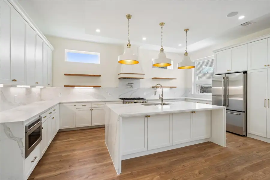 Kitchen features sleek white cabinetry, marble countertops, and stainless steel appliances. The open layout is complemented by wood flooring and stylish pendant lighting, creating a bright and inviting space.