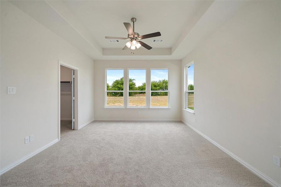 Unfurnished bedroom featuring a walk in closet, light carpet, a tray ceiling, and a ceiling fan