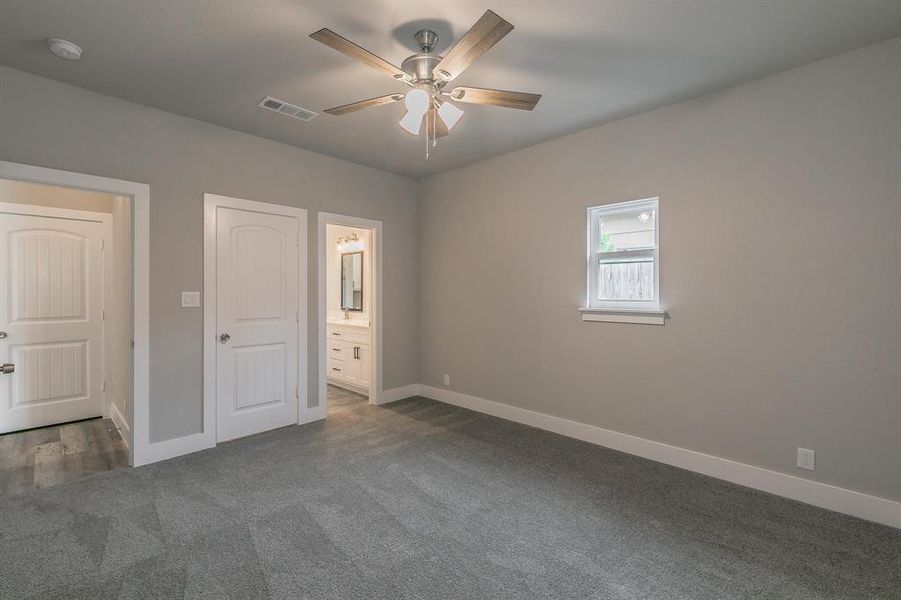 Primary bedroom with ceiling fan, dark colored carpet, and ensuite bathroom