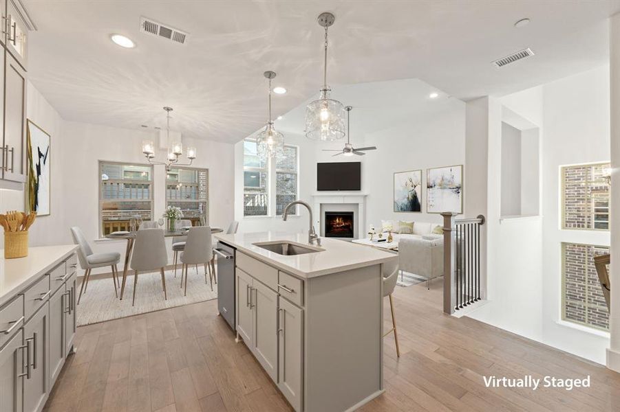 Kitchen featuring a lit fireplace, light wood finished floors, hanging light fixtures, an island with sink, and ceiling fan Kitchen featuring a lit fireplace, light wood finished floors, hanging light fixtures, an island with sink, and ceiling fan