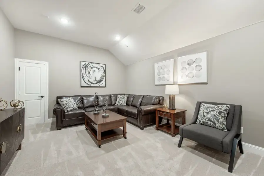 Living room with dark leather sectional sofa, gray accent chair, and vaulted ceiling over light carpet