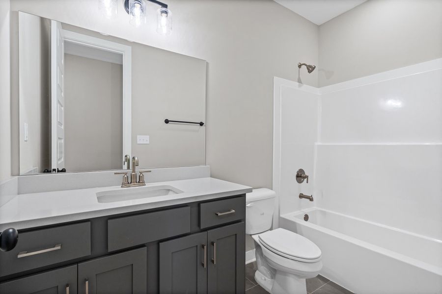 Full bathroom featuring a dark gray vanity with a light countertop and an integrated sink, brushed nickel faucet, large wall mirror, and a full-size bathtub with shower combination Full bathroom featuring a dark gray vanity with a light countertop and an integrated sink, brushed nickel faucet, large wall mirror, and a full-size bathtub with shower combination
