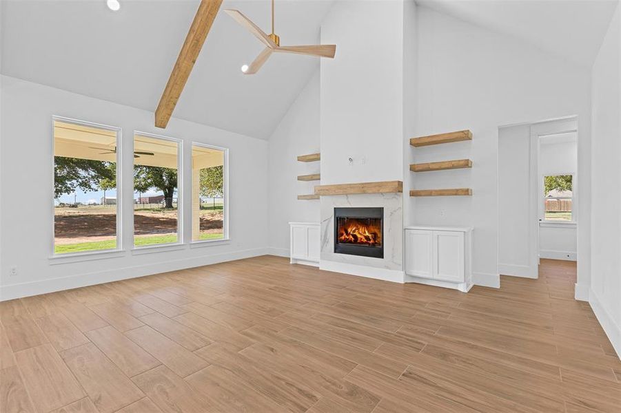 Unfurnished living room featuring high vaulted ceiling, a ceiling fan, a fireplace, light wood finished floors, and beamed ceiling