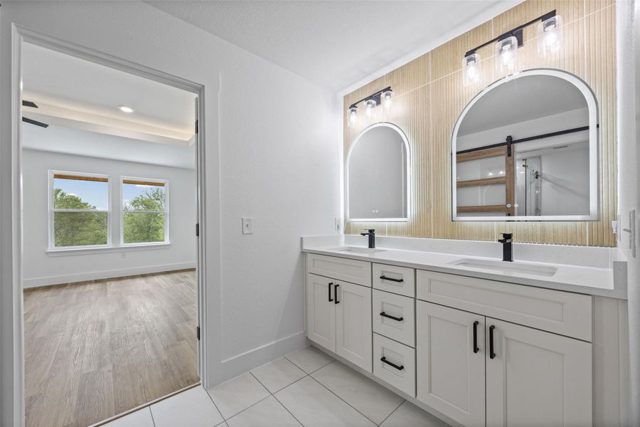 Dual vanity with white cabinetry, quartz countertops, black hardware, and arched backlit mirrors Dual vanity with white cabinetry, quartz countertops, black hardware, and arched backlit mirrors
