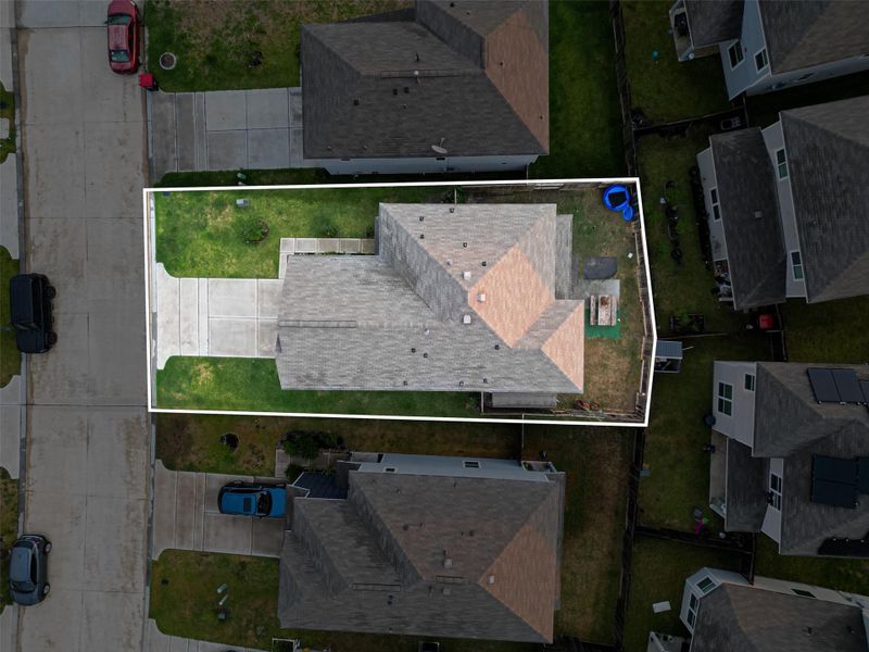 This aerial photo shows a well-maintained house with a fenced backyard, situated in a suburban neighborhood. It features a driveway leading to the property, surrounded by neighboring homes.