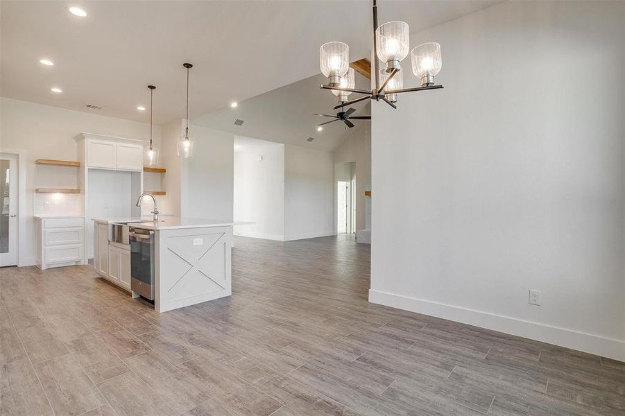 Kitchen featuring lofted ceiling, dishwasher, an island with sink, pendant lighting, and white cabinetry