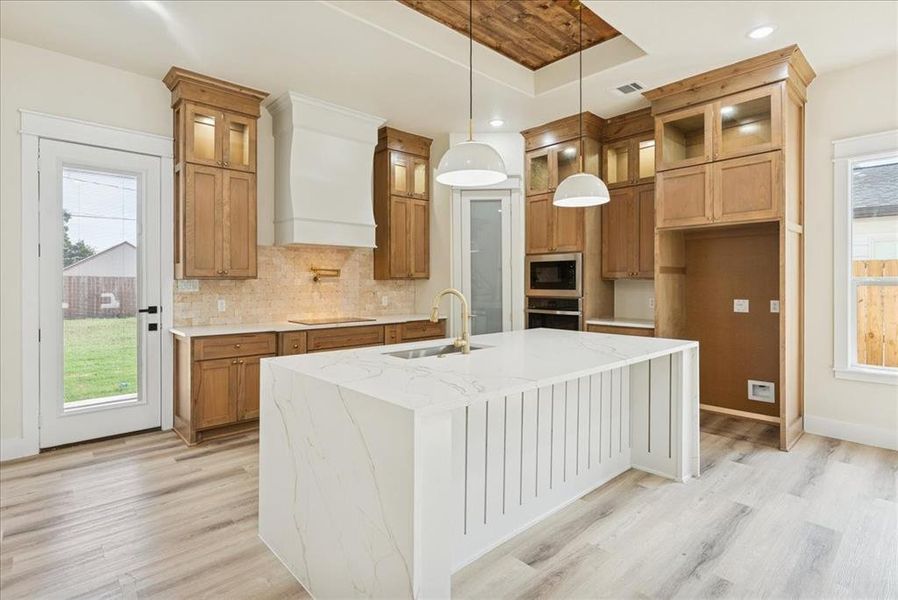 Kitchen with healthy amount of natural light, light stone counters, glass insert cabinets, tasteful backsplash, and recessed lighting
