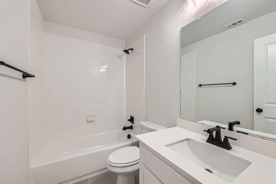 Full bathroom featuring vanity, tiled shower / bath combo, tile patterned floors, and toilet