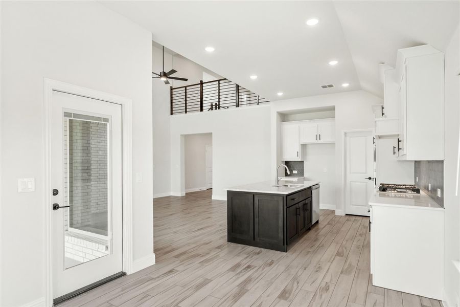 Open kitchen with dark island, white cabinets, light wood floors, and second-floor railing visible above.