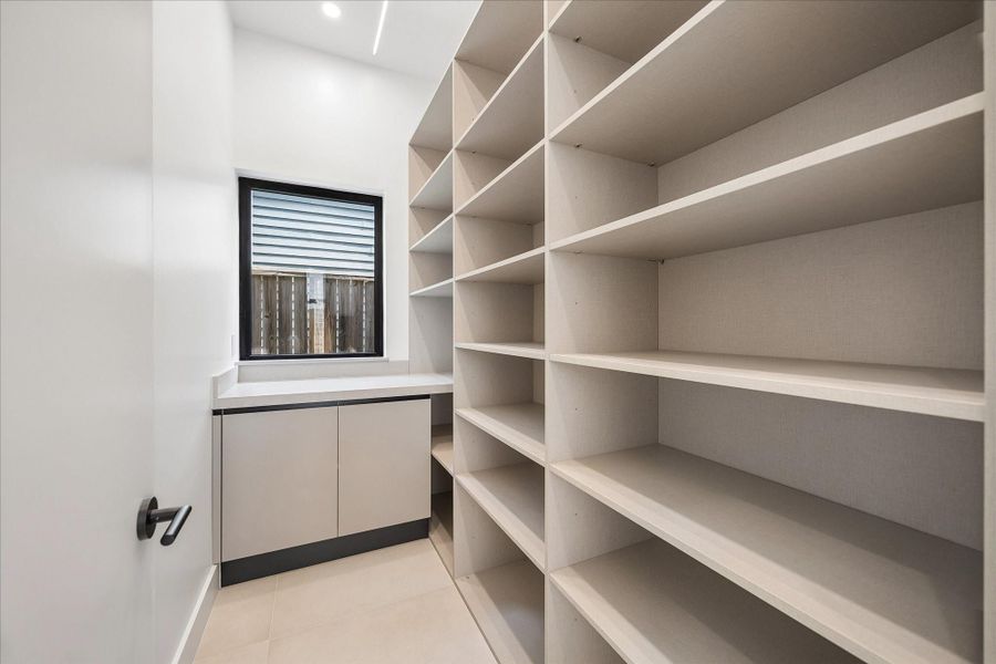 Walk-in pantry with ample shelving and an auxiliary countertop, featuring a window for natural light. Walk-in pantry with ample shelving and an auxiliary countertop, featuring a window for natural light.