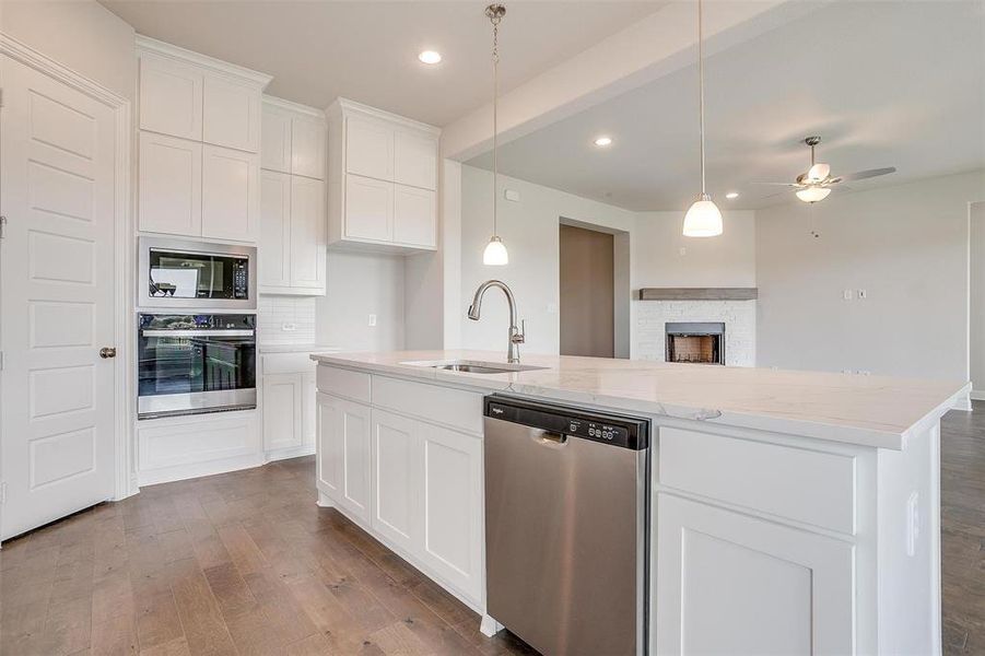 Kitchen with hardwood / wood-style floors, appliances with stainless steel finishes, white cabinetry, light stone countertops, and sink