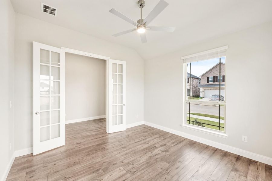 Empty room with hardwood floors, ceiling fan, and white French doors leading to a closet Empty room with hardwood floors, ceiling fan, and white French doors leading to a closet