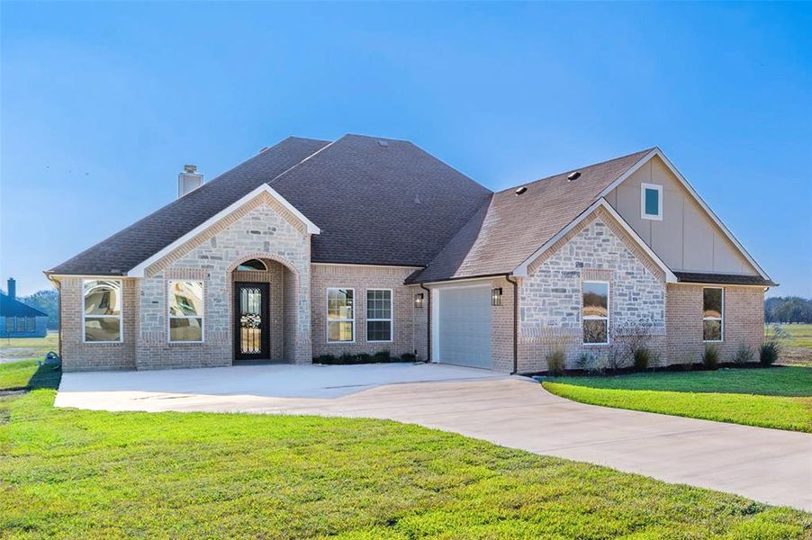 View of front of property featuring a front yard, stone siding, and driveway View of front of property featuring a front yard, stone siding, and driveway