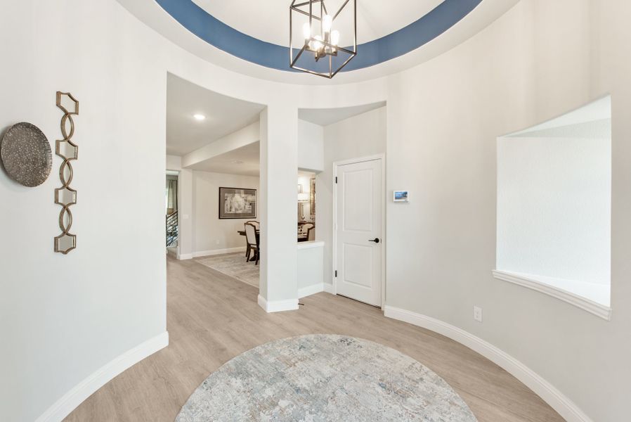 Curved foyer with round tray ceiling, blue accent, pendant light, and light hardwood floors