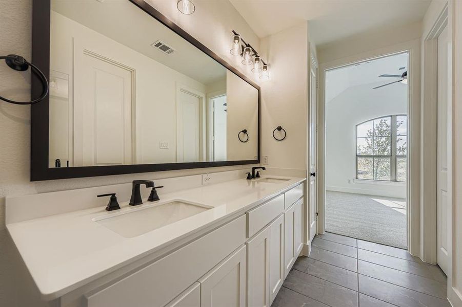 Bathroom with double vanity, dark tile patterned floors, dark colored carpet, and a ceiling fan