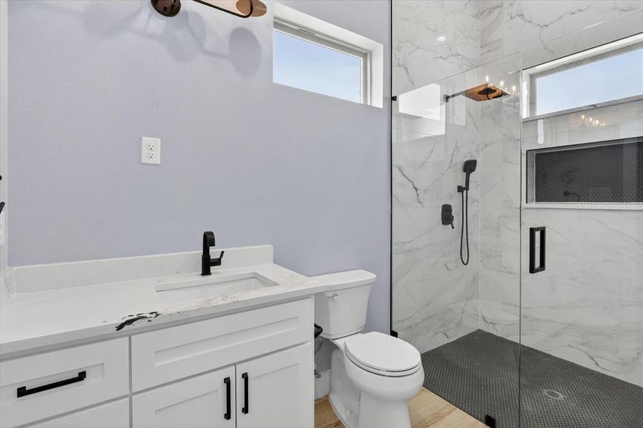 Bathroom featuring a glass-enclosed shower with black penny tile flooring and white marble-look wall tiling