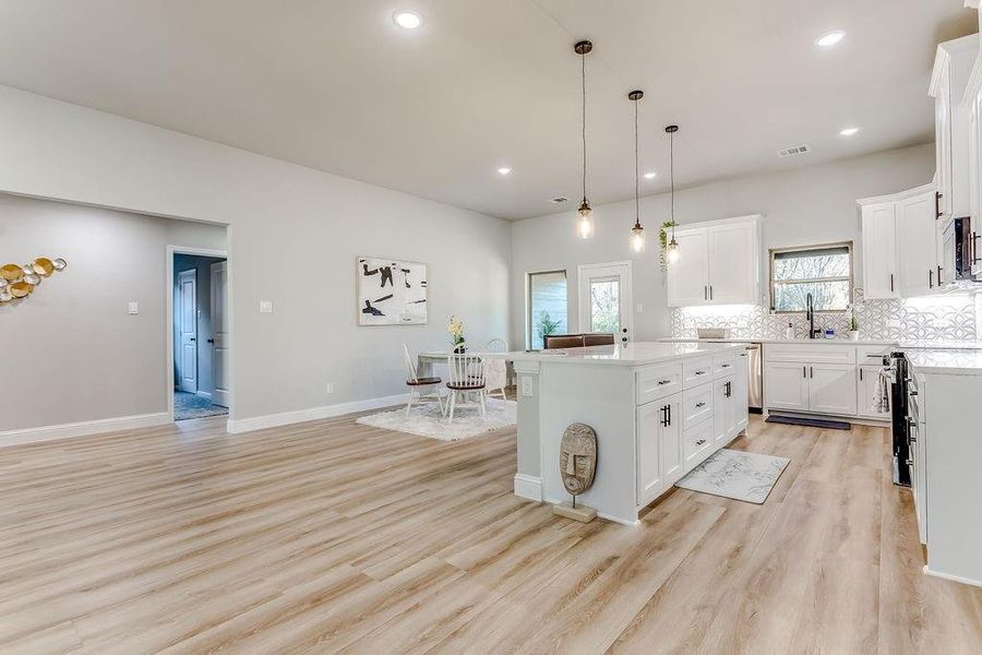 Kitchen featuring white cabinets, sink, light wood-type flooring, decorative light fixtures, and a kitchen island