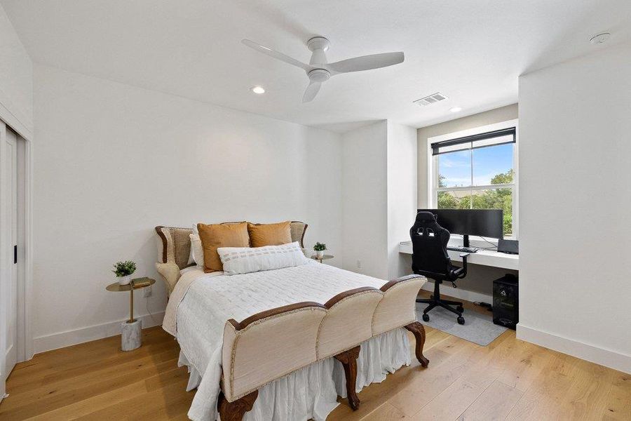 A well-lit bedroom features hardwood flooring and a dedicated workstation by the window, offering views of verdant trees. A well-lit bedroom features hardwood flooring and a dedicated workstation by the window, offering views of verdant trees.