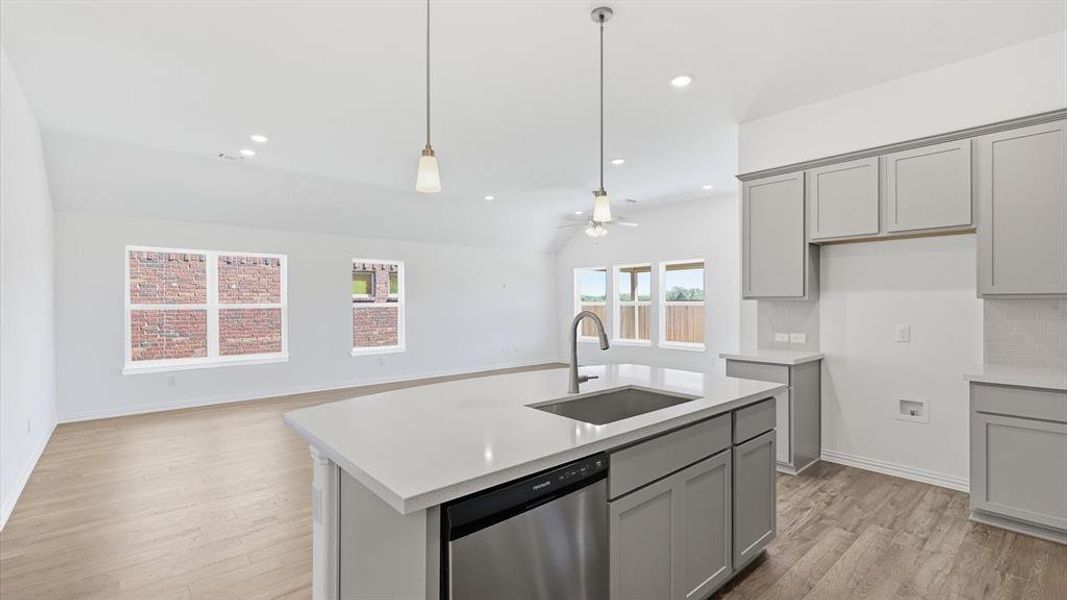 Open-concept kitchen featuring a large island with sink, stainless steel dishwasher, pendant lighting, shaker-style cabinetry, and light-toned countertops