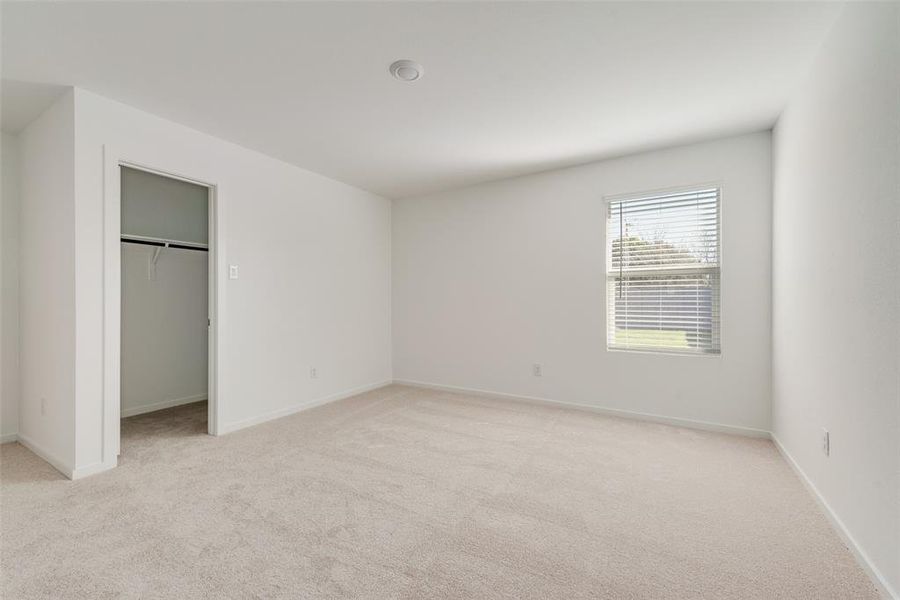 Unfurnished bedroom featuring a walk in closet, a closet, and light colored carpet