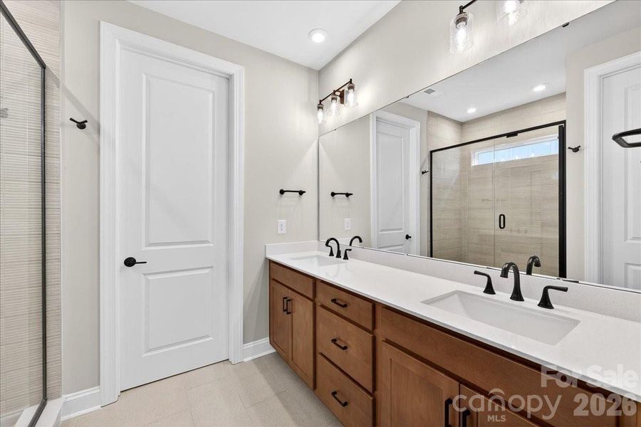Dual vanity primary bathroom with warm brown cabinets and white quartz countertops