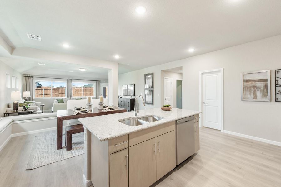 Open-concept kitchen with granite island, sink, and light wood cabinets overlooking dining and living areas with hardwood floors Open-concept kitchen with granite island, sink, and light wood cabinets overlooking dining and living areas with hardwood floors