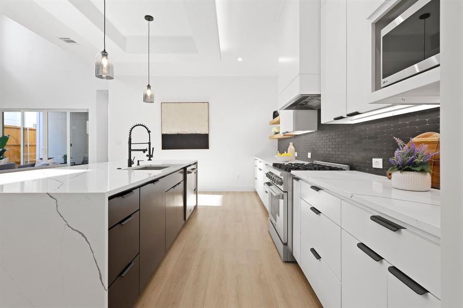 Kitchen with light wood-type flooring, a raised ceiling, hanging light fixtures, appliances with stainless steel finishes, and light stone counters