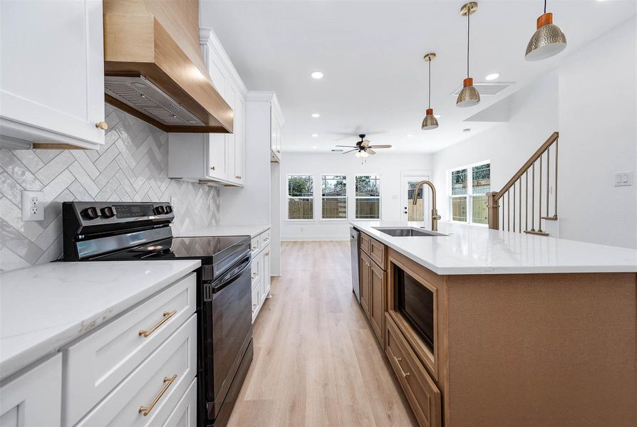 Open sightlines connect the kitchen to the living area, featuring quartz countertops, a custom wood vent hood, and elegant pendant lighting. Open sightlines connect the kitchen to the living area, featuring quartz countertops, a custom wood vent hood, and elegant pendant lighting.