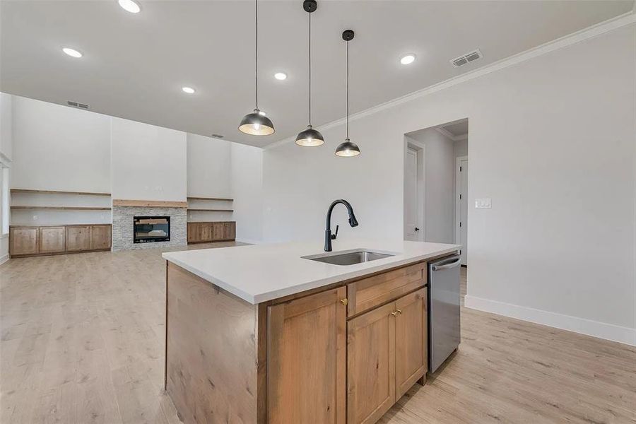Kitchen featuring open floor plan, a kitchen island with sink, a stone fireplace, pendant lighting, and light wood-style flooring