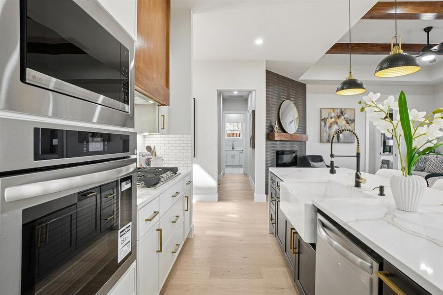 Kitchen featuring a fireplace, two tone cabinets, stainless steel appliances, light stone countertops, and decorative light fixtures