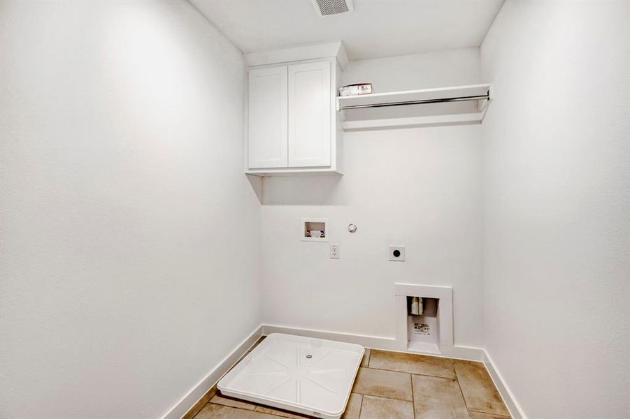 Dedicated utility space featuring white shaker-style cabinetry, a chrome hanging rod, and neutral tile flooring