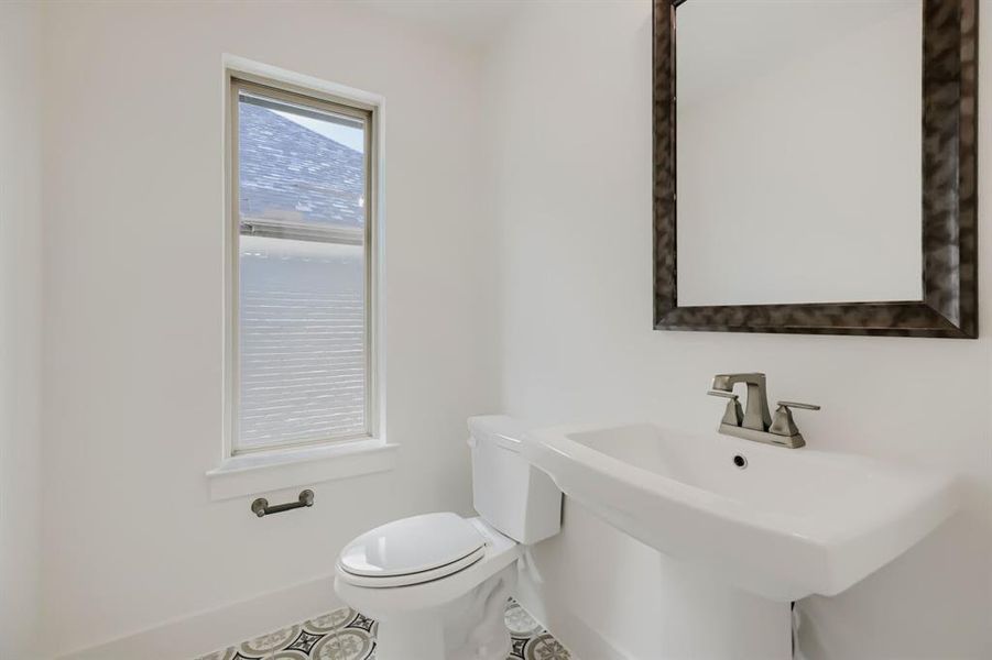 Pedestal sink with a brushed nickel faucet, framed mirror, and a window with blinds Pedestal sink with a brushed nickel faucet, framed mirror, and a window with blinds