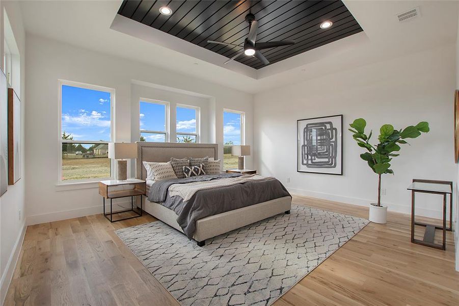 Bedroom with a tray ceiling, light wood-type flooring, and ceiling fan