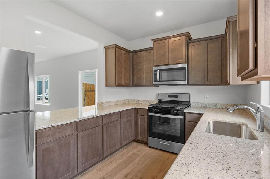 Kitchen with light wood-style flooring, kitchen peninsula, stainless steel appliances, sink, and light stone counters