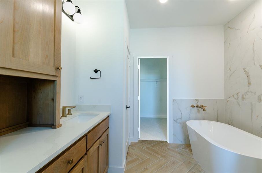 Full bathroom featuring vanity, a walk in closet, a soaking tub, and tile walls
