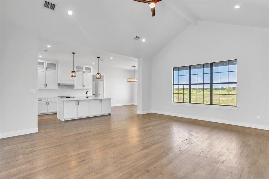 Unfurnished living room featuring beam ceiling, light hardwood / wood-style floors, sink, and high vaulted ceiling