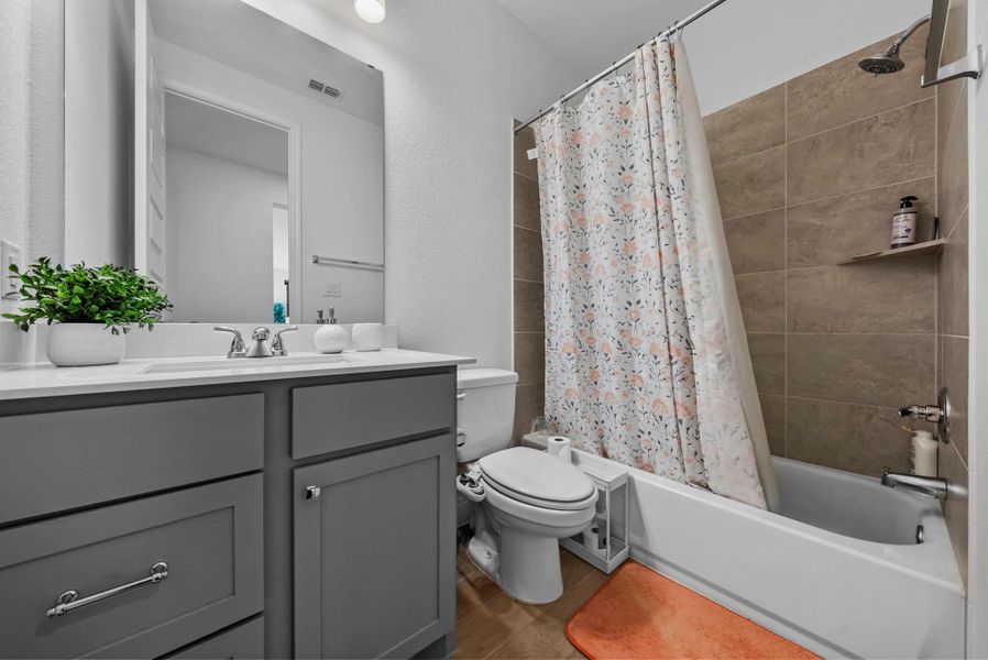 Full bathroom featuring shower / bath combination with curtain, vanity, and a textured wall