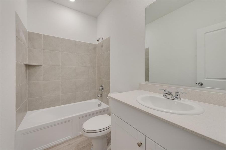 Full bathroom with hardwood / wood-style floors, tiled shower / bath, vanity, and toilet