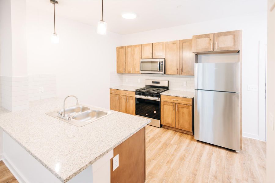 Kitchen featuring stainless steel appliances, a sink, a peninsula, tasteful backsplash, and light wood finished floors