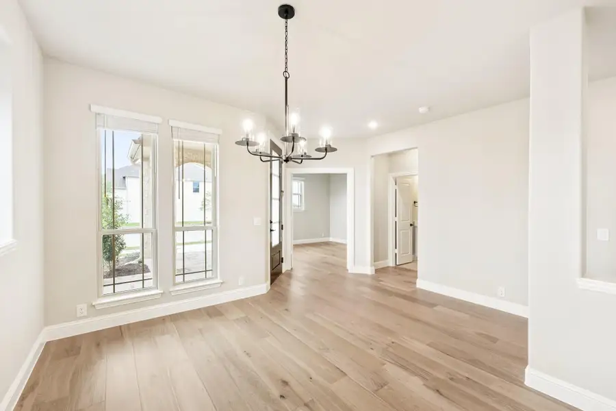 Empty dining room with light hardwood floors, black chandelier, and two large windows