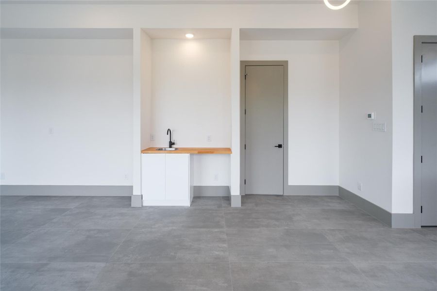 Representative Wet Bar View (Design selections and colors may vary): The built-in wet bar is neatly tucked in the living area featuring a white quartz countertop, sleek cabinetry and a modern faucet. Large cement-like gray tiles flooring is one of the select upgrades incorporated into a different unit.