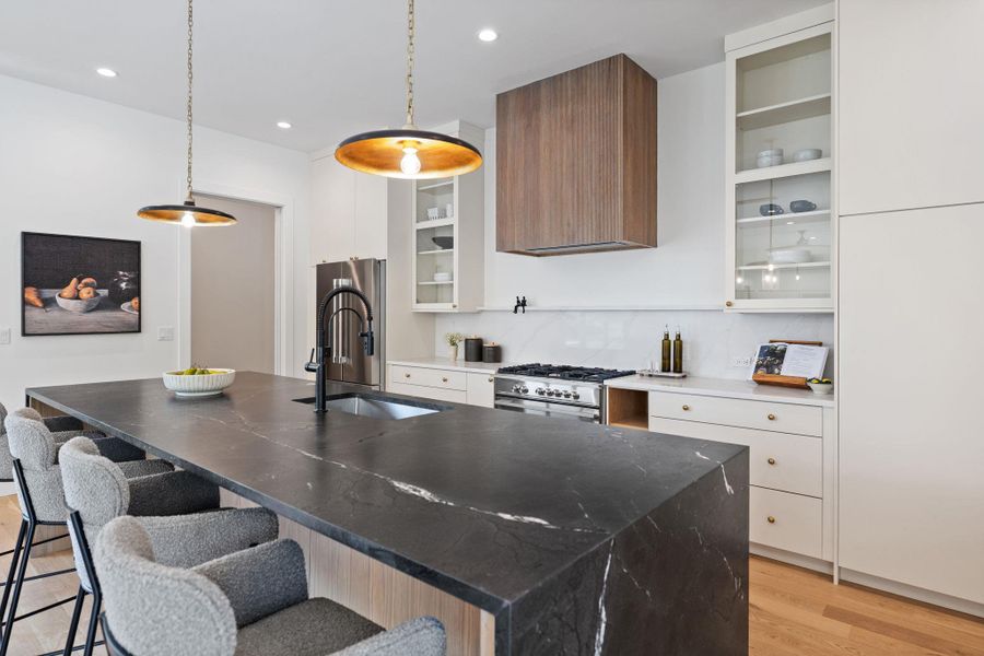 Kitchen featuring white cabinets, light wood-type flooring, a kitchen island with sink, decorative backsplash, and hanging light fixtures Kitchen featuring white cabinets, light wood-type flooring, a kitchen island with sink, decorative backsplash, and hanging light fixtures