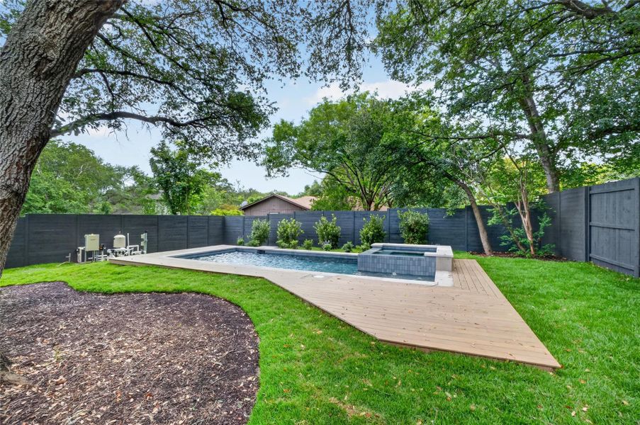 An inviting backyard oasis awaits with a sparkling pool and spa, framed by mature trees and lush greenery.