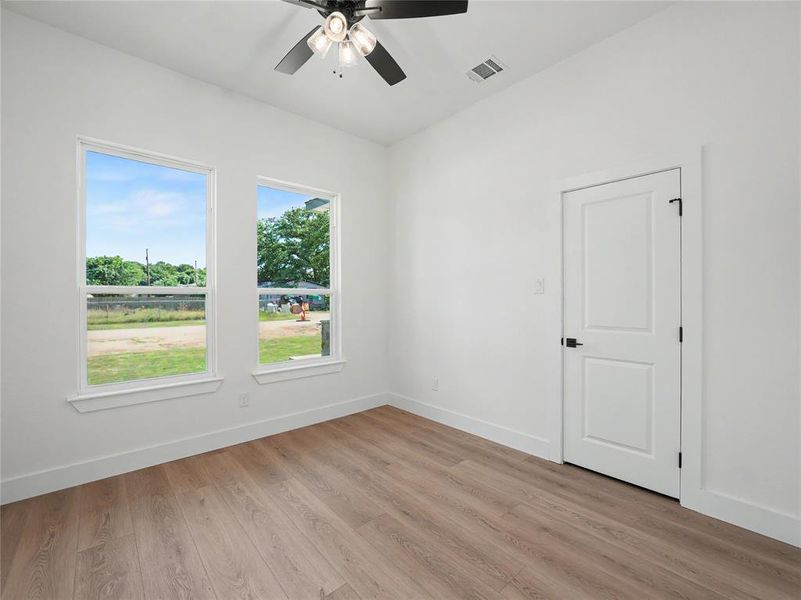 Interior room featuring wood-finish flooring, two large windows, a ceiling fan with light fixture, and a white paneled door with black hardware Interior room featuring wood-finish flooring, two large windows, a ceiling fan with light fixture, and a white paneled door with black hardware