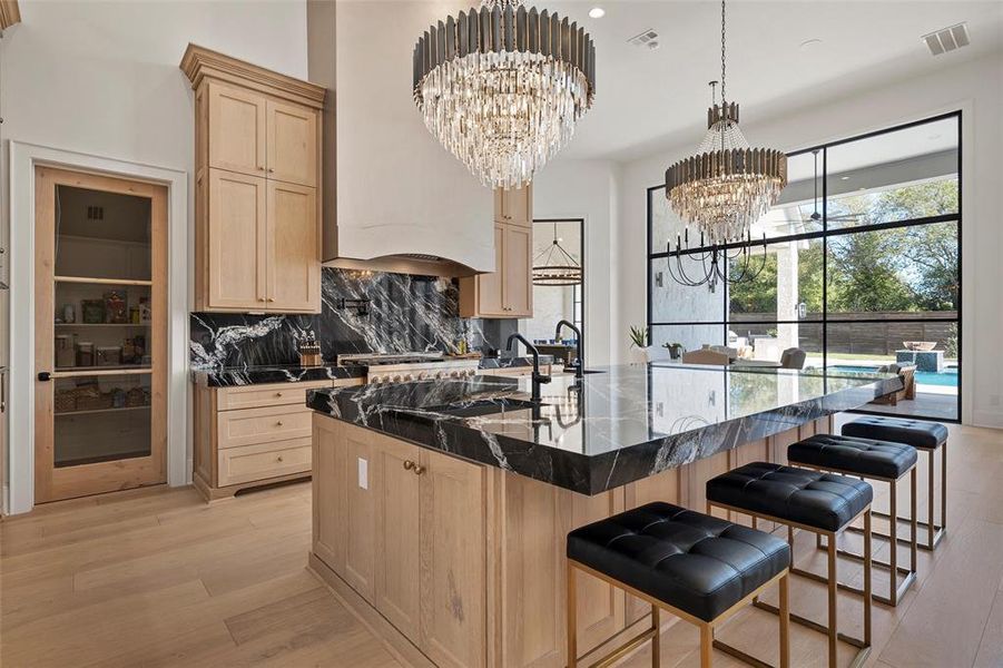 Kitchen with light brown cabinetry, a kitchen bar, backsplash, a center island with sink, and dark stone countertops
